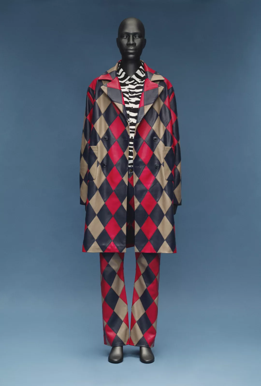 A mannequin dressed in a black and red and gold harlequin style coat and trousers with a leopard print shirt