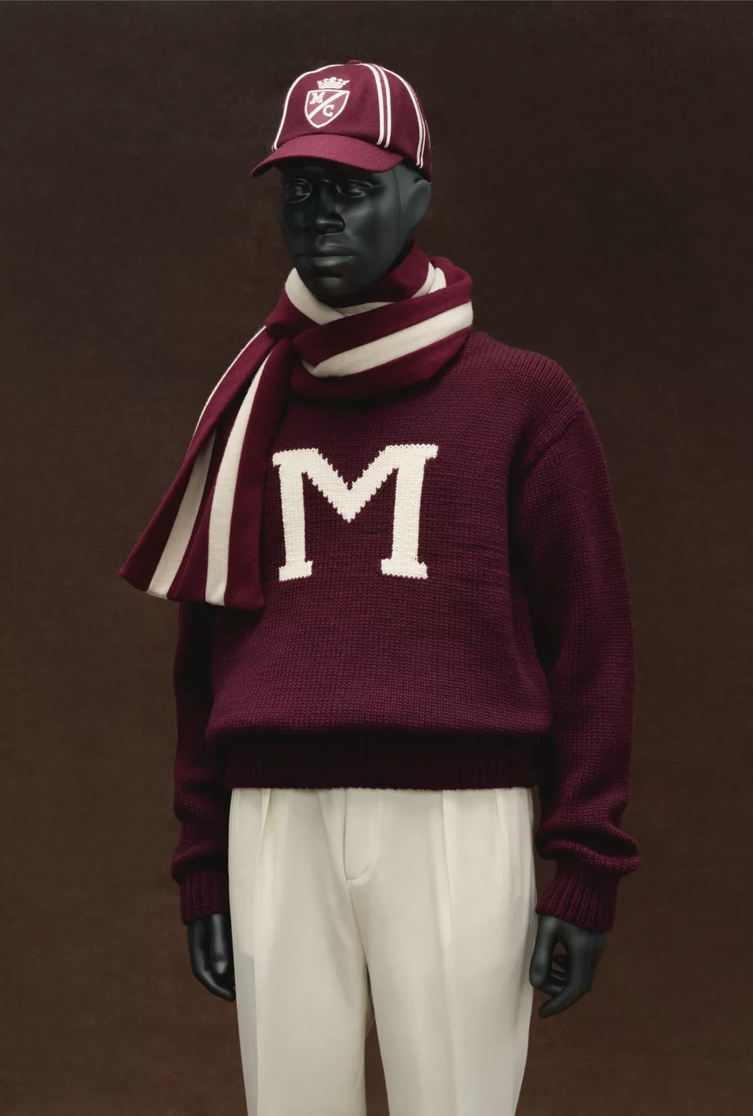 A mannequin dressed with a burgundy coloured cap, jumper and cream trousers