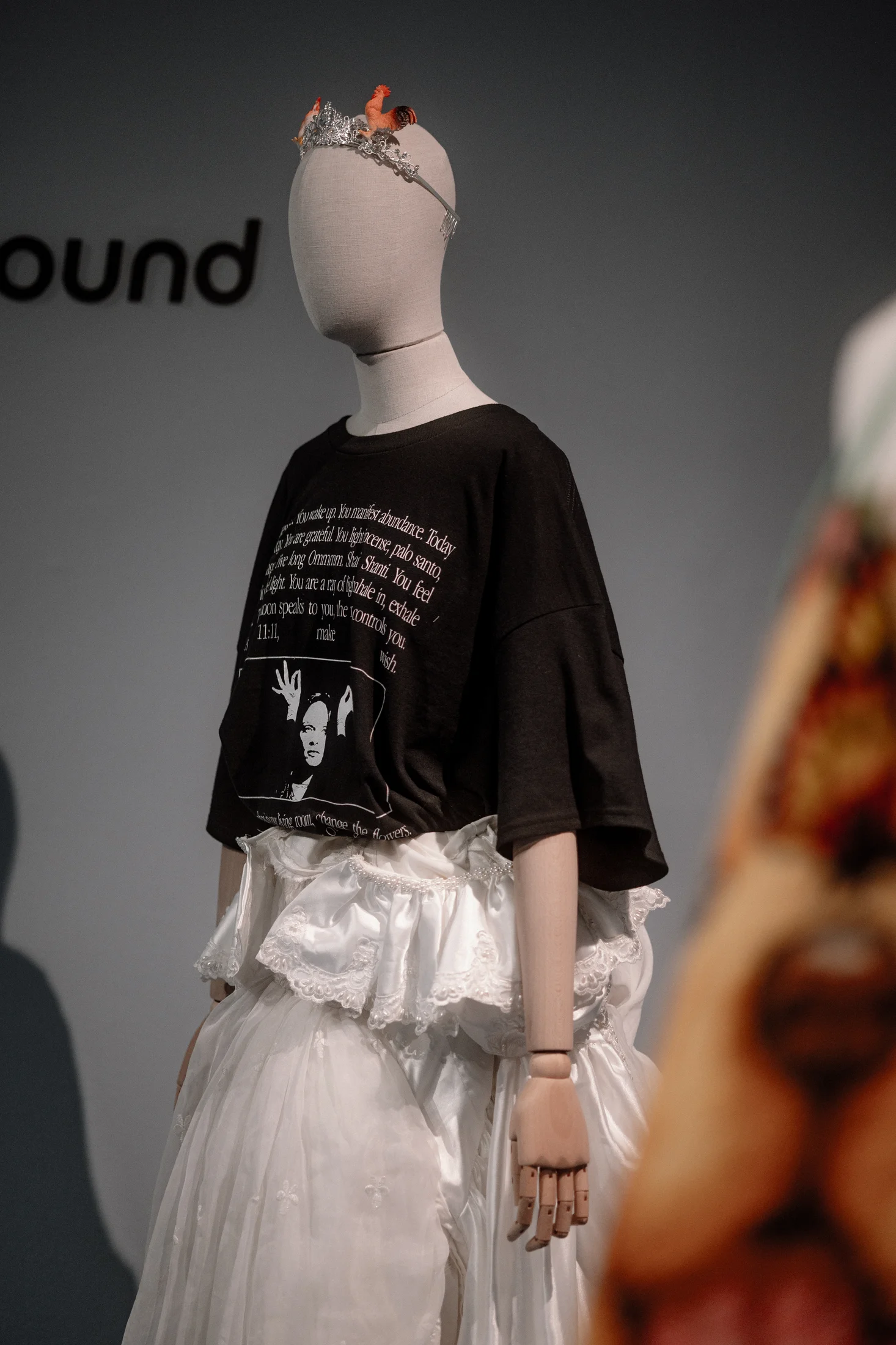 Mannequin wearing a black graphic t-shirt over a white ruffled full-length skirt, topped with a small wire crown