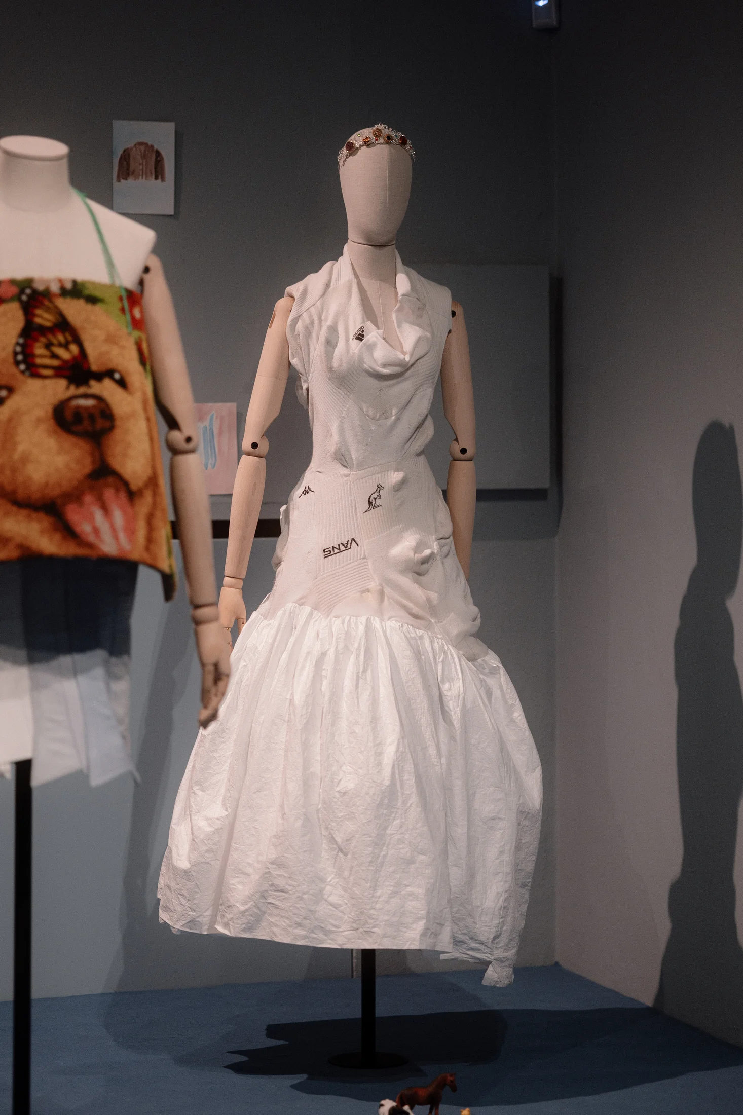 Mannequin wearing a white deconstructed dress made from repurposed sportswear fabrics featuring Kappa, Vans, and Australian logos
