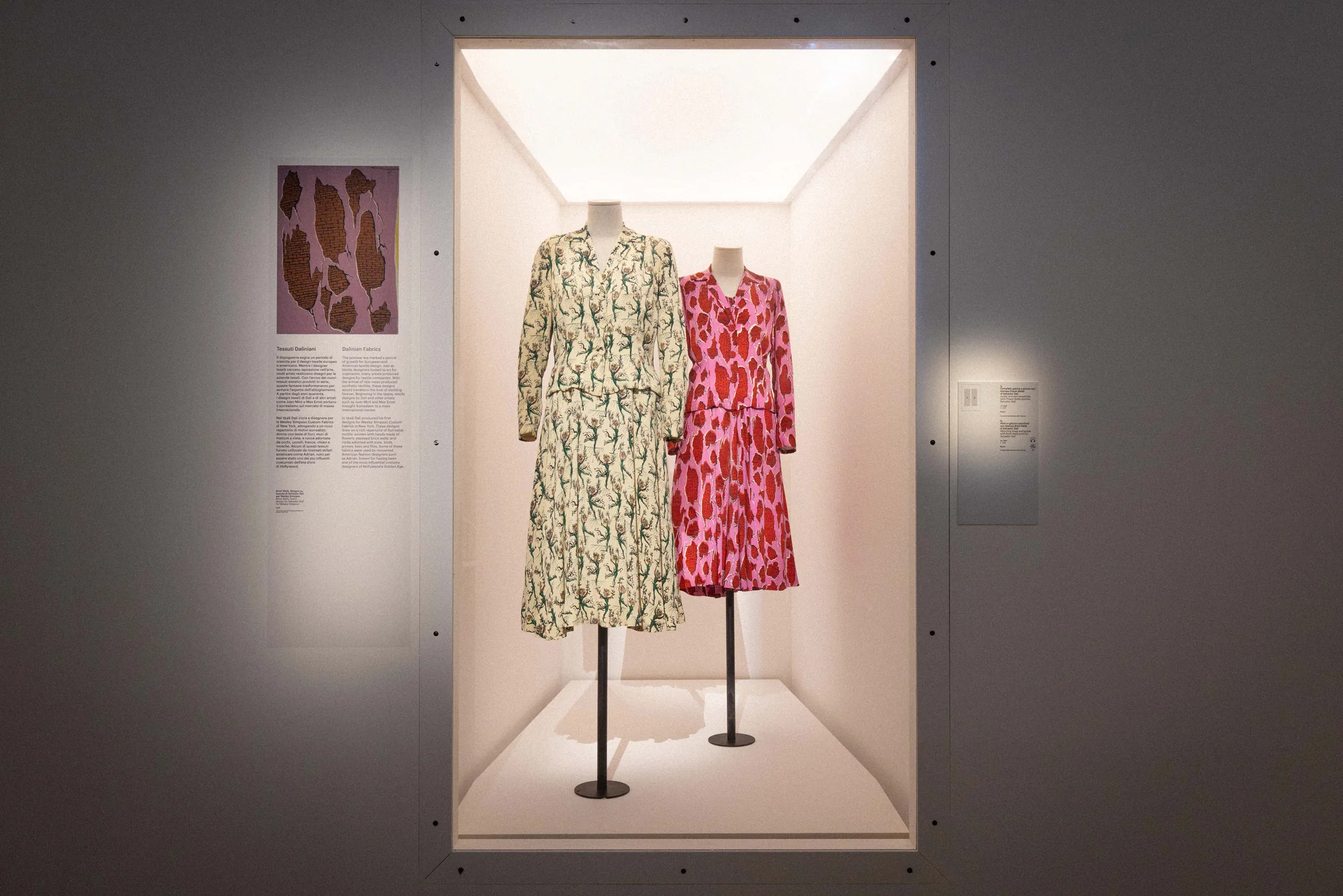 Two printed dresses, one cream and one pink, displayed in a lit white niche