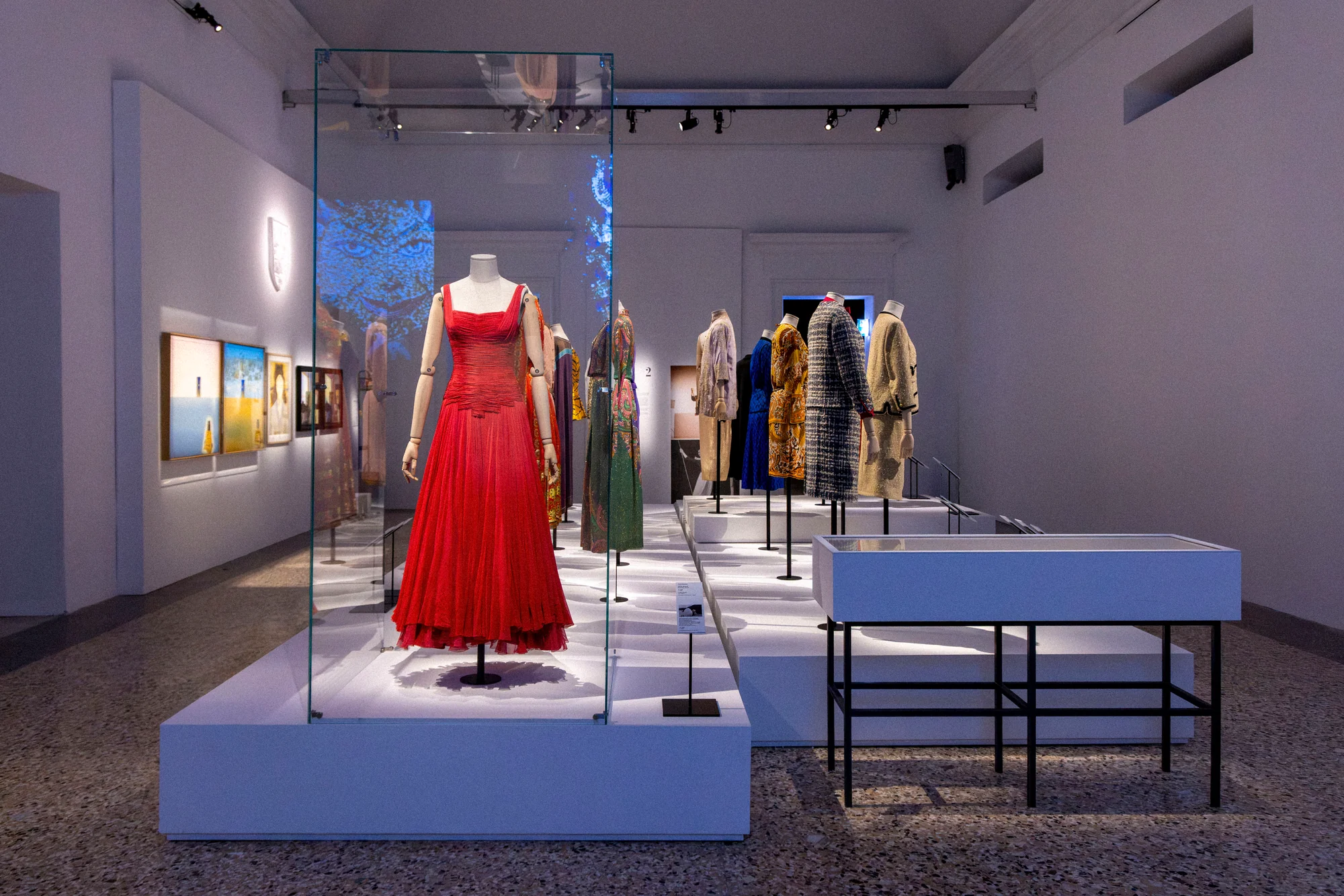Exhibition hall with a red gown in a glass case and a row of colourful coats on a long white plinth