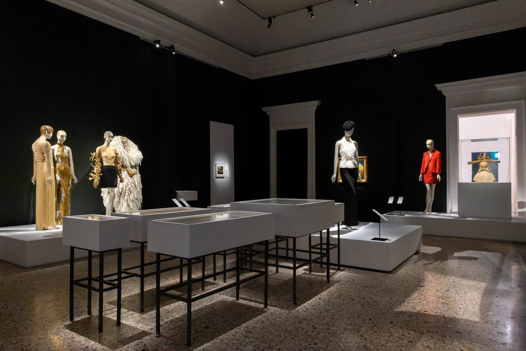 Dark gallery with display tables and mannequins in gold, white and red outfits