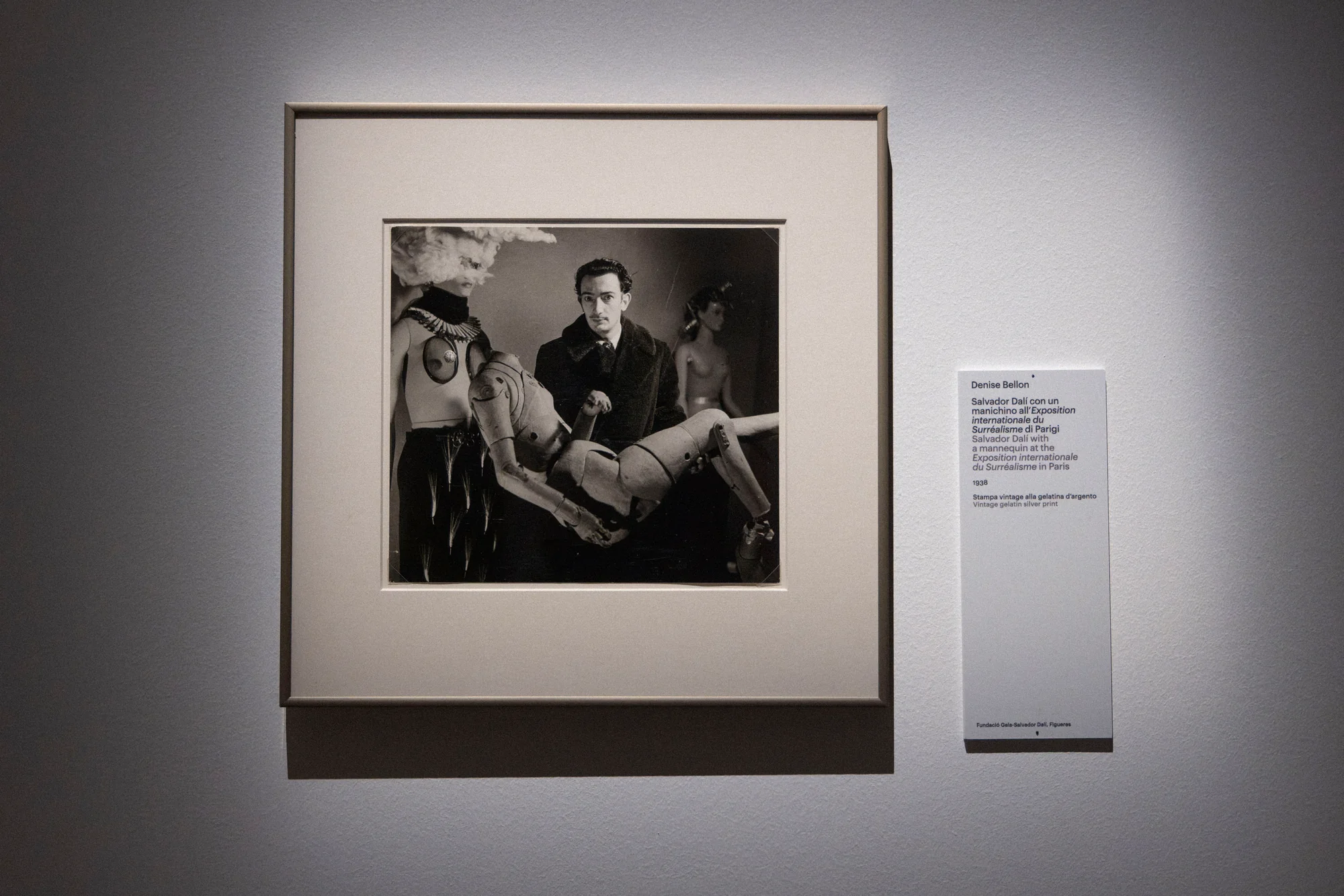Framed black-and-white photograph of a man holding a mannequin, with a caption on the wall