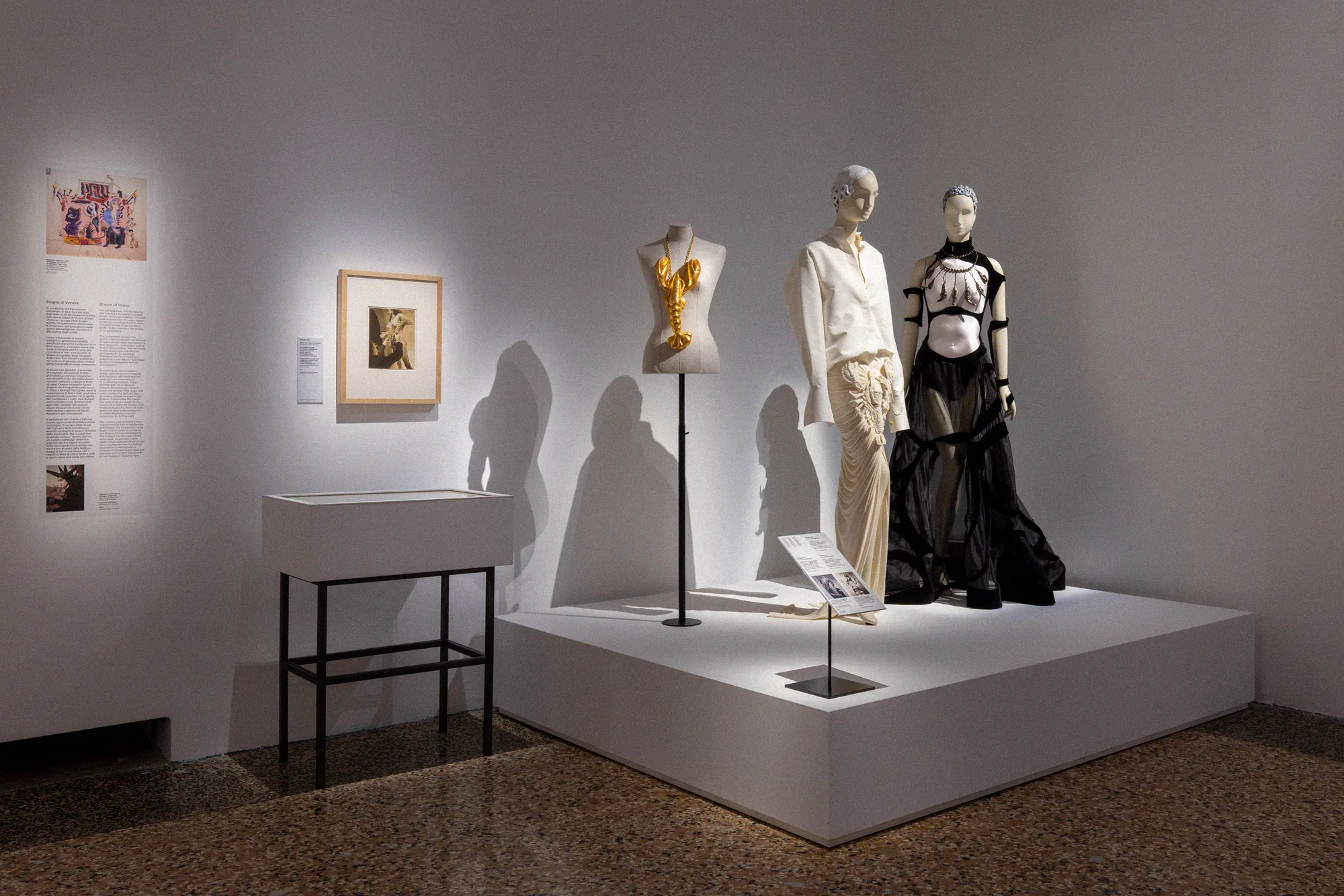 Plinth with a gold bodice on a stand and mannequins in a white trouser suit and a black sheer gown