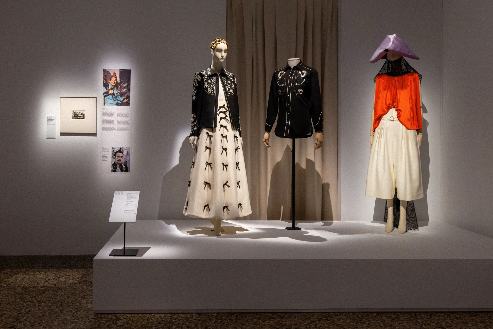 Mannequins in an embroidered black jacket with white skirt, a black shirt and an orange top with a pointed hat