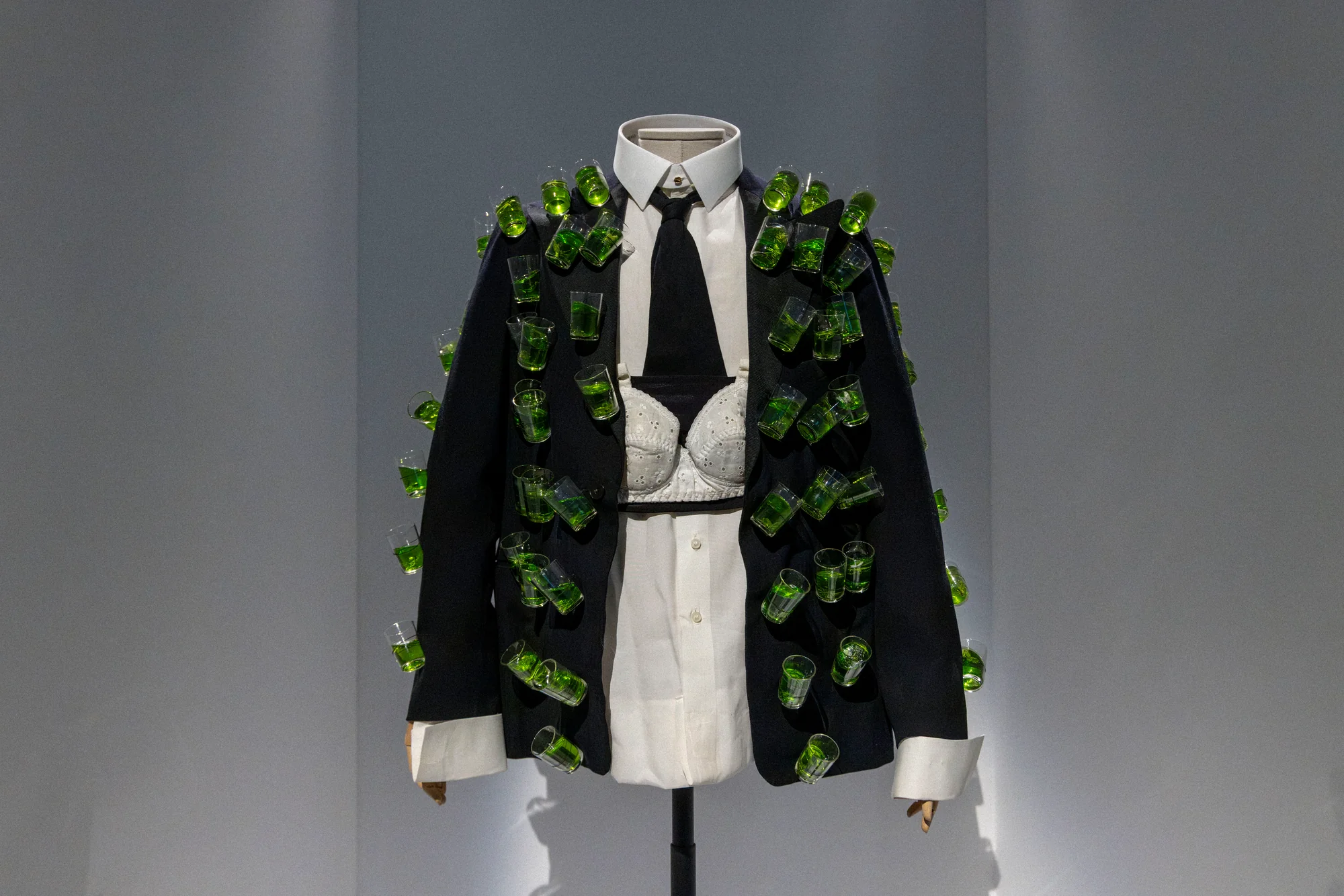 Black jacket covered in small glasses of green liqueur, over a white shirt and black tie