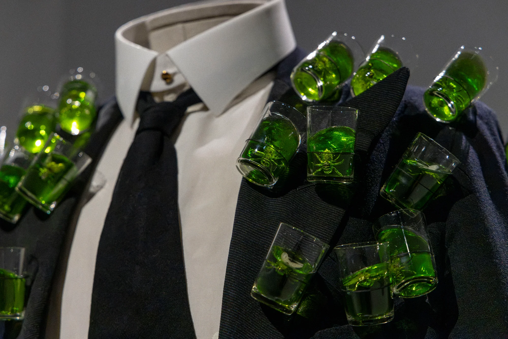 Close-up of glasses of green liqueur attached to a black jacket over a white shirt and tie