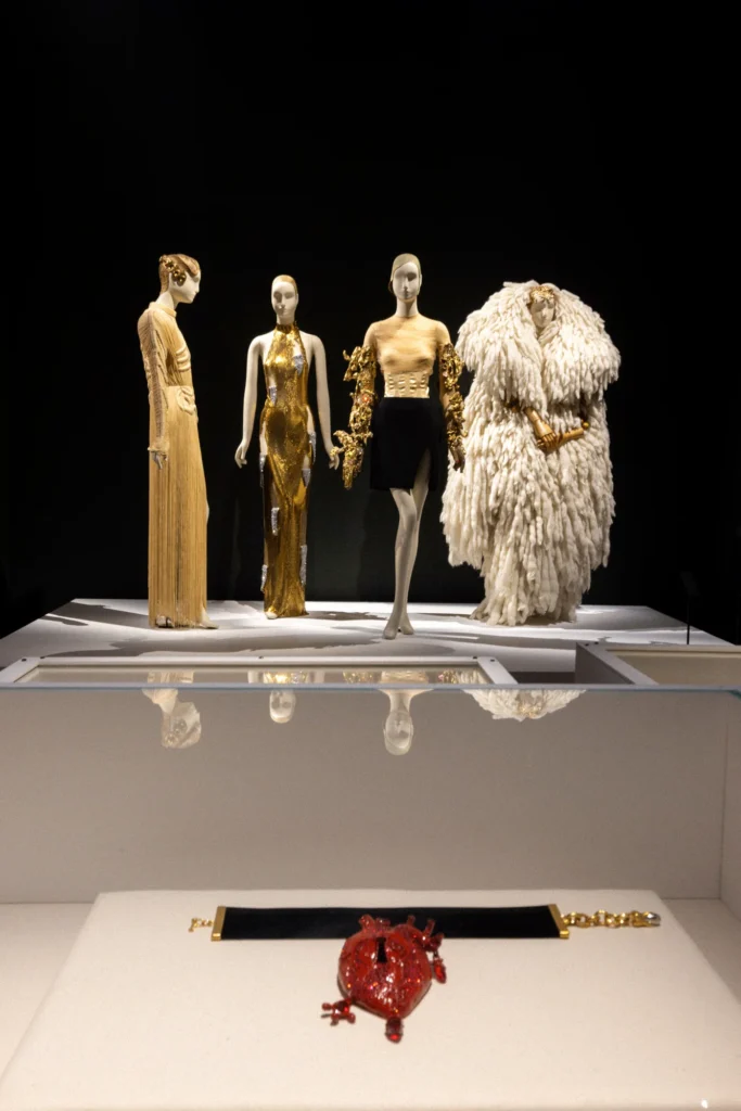 Mannequins in gold and feathered outfits behind a glass case holding a ruby heart brooch