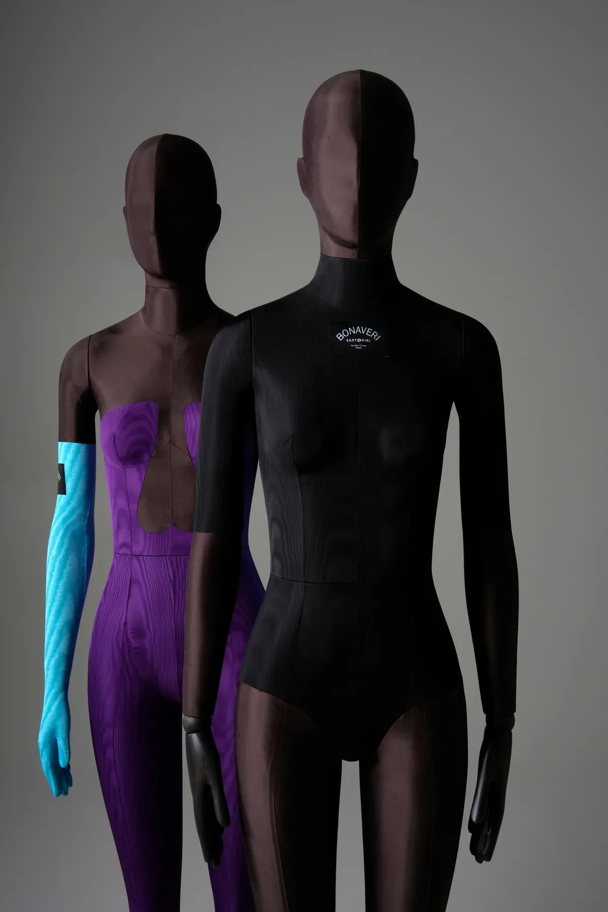 Two Bonaveri Sartorial Bespoke mannequins side by side: the purple jumpsuit with blue gloves and the black moire bodysuit with Bonaveri branding
