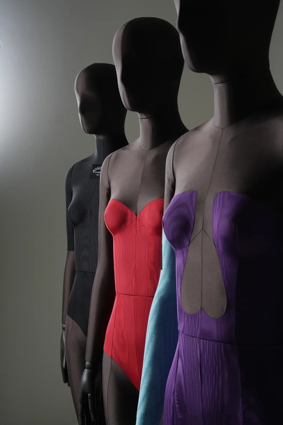 Close-up of three Bonaveri Sartorial Bespoke mannequin torsos showing the black bodysuit, red corset, and purple jumpsuit moulage upholstery details
