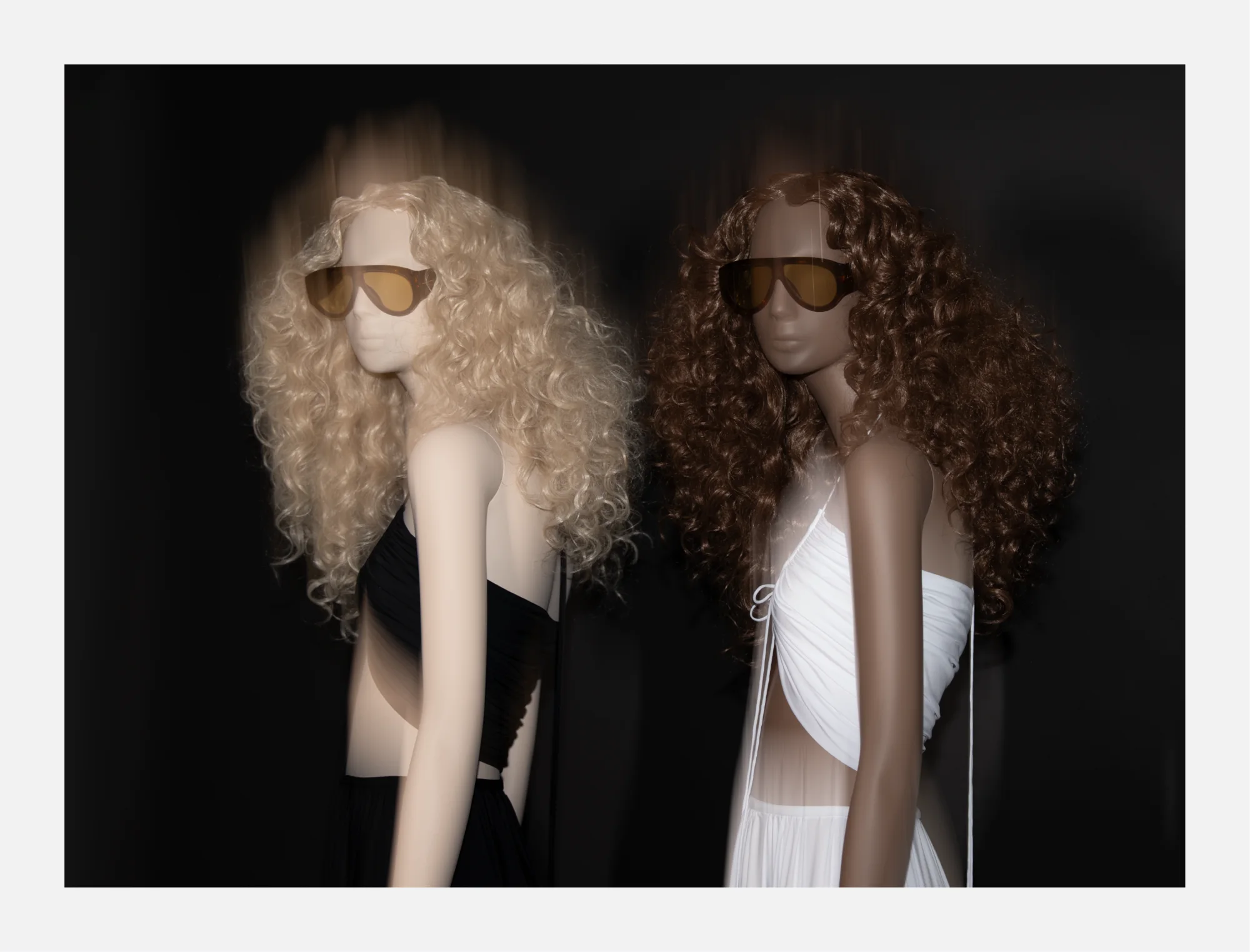 Two Obsession mannequins with blonde and brunette curled wigs