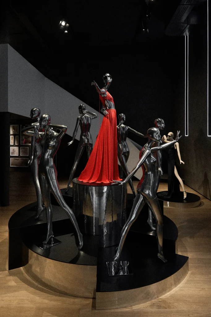 Chrome mannequins on a round mirrored plinth around a red Halston-inspired gown