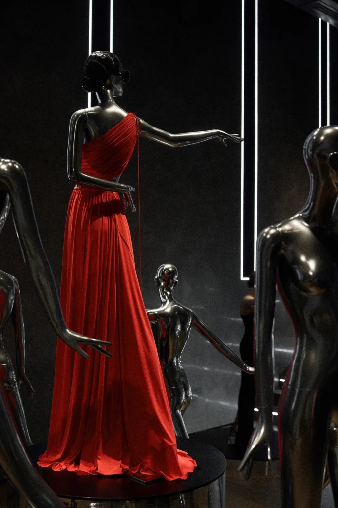 Chrome mannequin in a long red one-shoulder gown among chrome figures