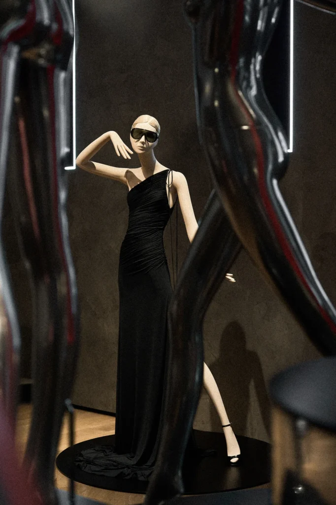 Mannequin in a black one-shoulder gown and sunglasses, framed by chrome figures