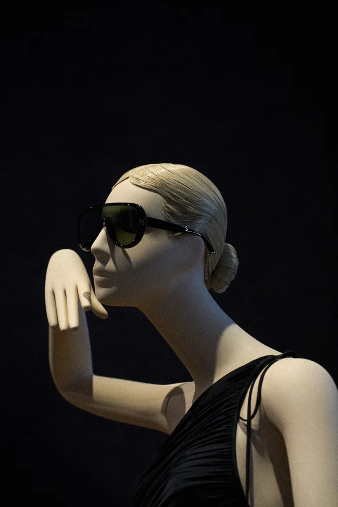 Close-up of a blonde mannequin in sunglasses with a hand raised to its face