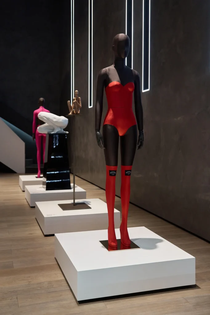 Mannequins on white plinths in the showroom, one in a red bodysuit and red stockings in front