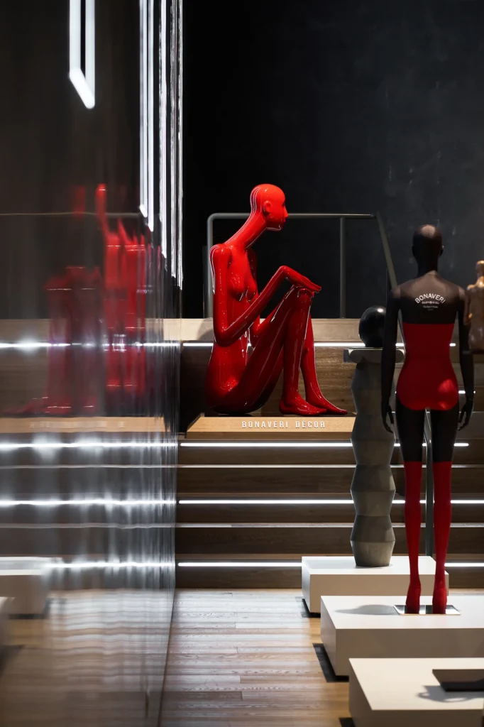 Red seated figure on lit steps beside a mannequin in a red bodysuit and red stockings