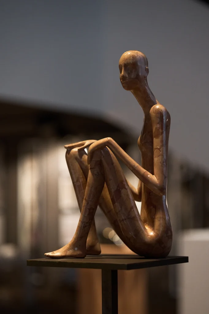 Wooden figure seated with its knees drawn up, on a dark stand
