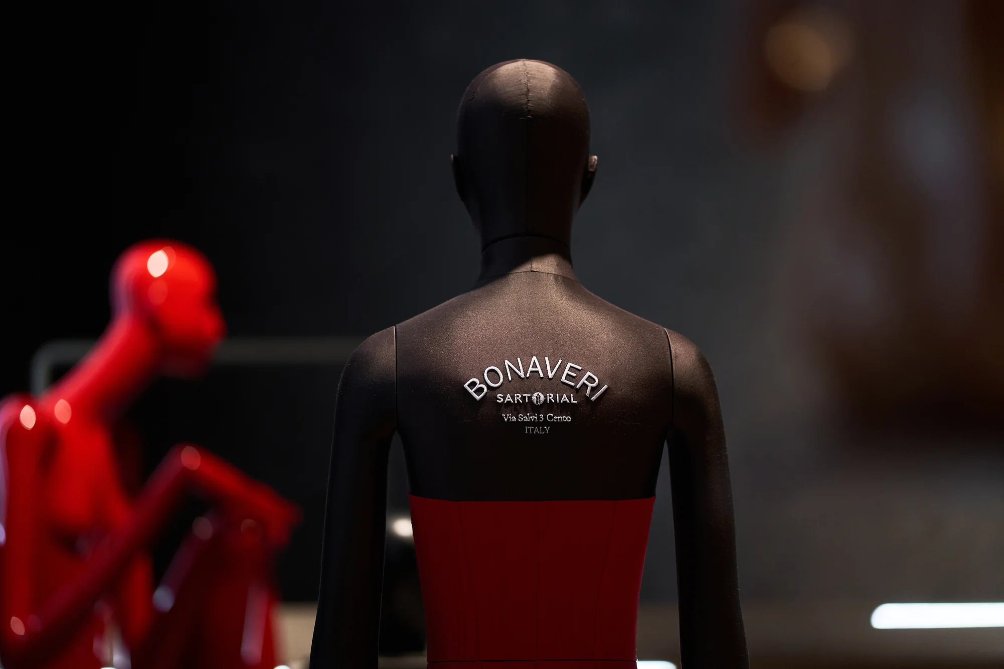 Mannequin seen from behind with the Bonaveri Sartorial logo on its back, a red seated figure beside it